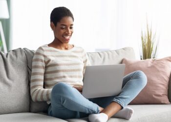 Freelance Career. Millennial Black Female Working With Laptop Computer At Home, Smiling Young African American Lady Sitting On Couch In Living Room And Typing On Keyboard, Enjoying Remote Work