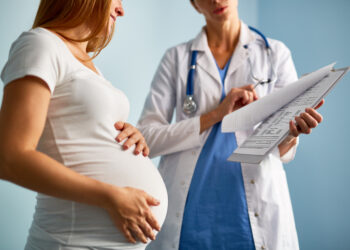 Pregnant female looking at paper with medical prescriptions held by her therapeutist