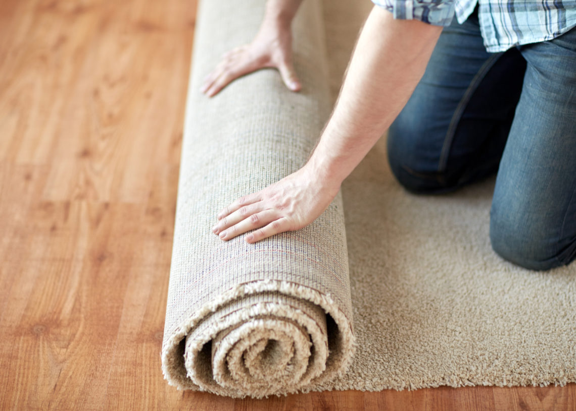 repair, building and home concept - close up of male hands rolling carpet