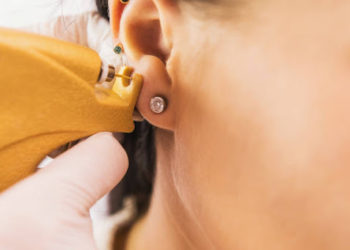 A doctor in sterile white medical gloves pierces the ears of a young girl in the medical office with a piercing gun. High quality photo