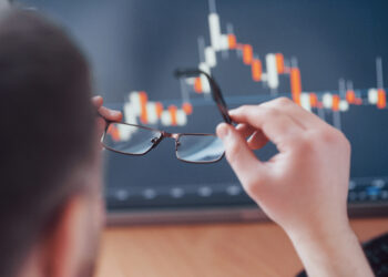 Analyzing data. Close up of a young businessman who holds glasses and looks at the gff while working in a creative office.